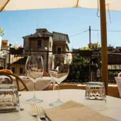 Tavola apparecchiata con bicchieri e posate in un ristorante all'aperto, con vista sui tetti di Roma. Un'atmosfera perfetta per scoprire i migliori ristoranti di Roma.