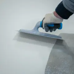 Ręka w rękawicy wyrównuje wylewkę na balkonie za pomocą kielni.