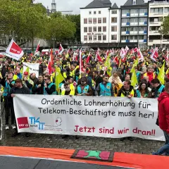 Große Menschenmenge bei einem Telekom-Streik. Sie fordern "Ordentliche Lohnerhöhung für Telekom-Beschäftigte muss her!". Viele Fahnen und gelbe Westen sind zu sehen.
