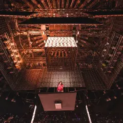 Billie Eilish na scenie, otoczona skomplikowaną konstrukcją oświetleniową. Tekst piosenki "NDA" rozbrzmiewa w tłumie.