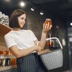 Kobieta w sklepie z koszykiem zastanawia się, czy ten miód to nie fałszowanie.