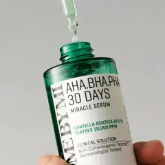 En droppe serum från en pipett landar på en flaska med "AHA.BHA.PHA 30 DAYS MIRACLE SERUM", en effektiv hudvård mot akne.