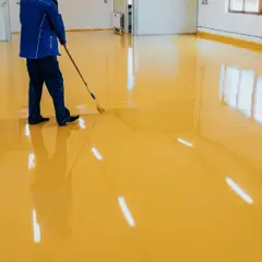 Operaio stende resina poliuretanica o epossidica gialla su un pavimento lucido, creando un ambiente moderno e resistente.