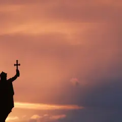 Silueta de estatua con cruz alzada, evocando la gesta de Don Pelayo y la Reconquista, bajo un cielo crepuscular.