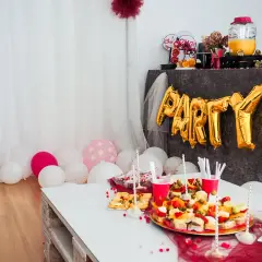 Urocze pomysły na wieczór panieński w domu: złote balony z napisem "PARTY", przekąski i różowe akcenty.
