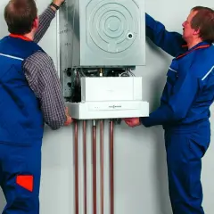 Dwóch techników montuje kocioł gazowy, zapewniając jego zabezpieczenie pieca gazowego przed przepięciem.