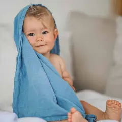 Ein süßes Baby von 12 Monaten, eingewickelt in ein blaues Tuch, schaut neugierig in die Kamera.