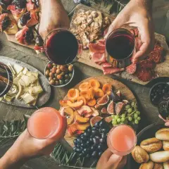 Idealne, tanie przekąski na imprezę: deska serów, owoców, wędlin, oliwek i mini bułeczek. Wszyscy wznoszą toasty!