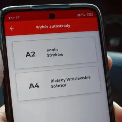 Dłoń trzyma smartfon z aplikacją do wyboru autostrady A2 Konin-Stryków i A4 Bielany Wrocławskie-Sośnica.