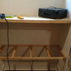 DIY project: a drill, level, and audio receiver sit on a wooden shelf, with a frame for another shelf below, showing how to hang shelves.