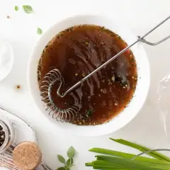 Przygotowanie marynaty do mięsa w solance. W misce brązowy płyn z ziołami i przyprawami, obok sól, pieprz, czosnek i surowe mięso w woreczku.