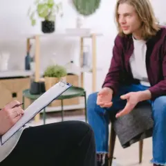En person sitter och skriver på en clipboard medan en annan person pratar. En scen som kan symbolisera tvångstankar behandling.