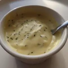En skål med krämig, gul vegansk bearnaisesås med finhackade örter. Perfekt för ditt veganska bearnaisesås recept.