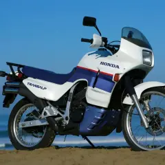 Biało-niebieski motocykl Honda Transalp 650 stoi na plaży.