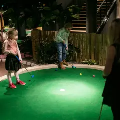 Barn spelar minigolf inomhus i Stockholm. En tropisk miljö med bambustaket och palmer.