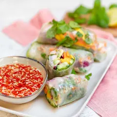 Färska vietnamesiska vårrullar fyllda med grönsaker och räkor, serverade med en röd dippsås.