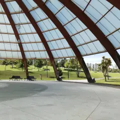 Estructura de madera y cristal en el parque de Eiris, con vistas a césped, árboles y edificios.