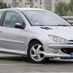 Srebrny Peugeot 206 na mokrym parkingu, z widocznym numerem rejestracyjnym WN 4933C.