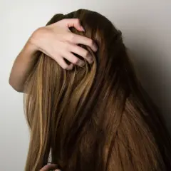 En person med långt, brunt hår som kliar sig i hårbotten, kanske på grund av biotin brist.