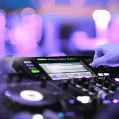 Mano che mixa su console DJ, luci viola e rosa sfocate creano l'atmosfera perfetta per la techno house music.
