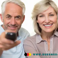 Glückliches Rentnerpaar mit Fernbedienung. Informieren Sie sich über die GEZ-Befreiung für Rentner und die Einkommensgrenze auf www.buerger-geld.org.