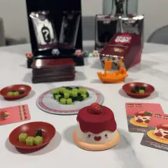 Gra Sushi Go Party! z uroczym puddingiem truskawkowym i kostkami do gry.