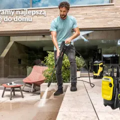 Mężczyzna używa myjki ciśnieniowej na tarasie obok żółtych urządzeń Karcher.