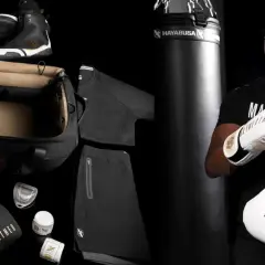 Floyd Mayweather Jr. smiles, holding a pair of white and gold Mayweather boxing gloves. The image also displays his boxing gear, including black gloves, shoes, and apparel.