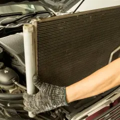 Mechanik wyjmuje chłodnicę klimatyzacji. Sprawdź wymiana chłodnicy klimatyzacji cena.