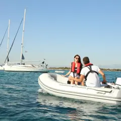 Coppia su una tender barca, con vele bianche all'orizzonte.