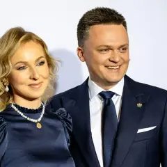 Szymon Hołownia z żoną, uśmiechnięci, pozują do zdjęcia. Ona w granatowej sukience i perłach, on w garniturze.