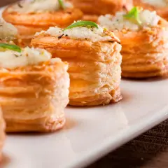 Petites bouchées à la reine dorées, garnies d'une préparation crémeuse et d'une feuille de basilic, présentées sur un plat blanc.
