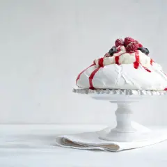 En vacker pavlova i långpanna, toppad med grädde, bär och röd sås.