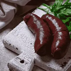 Deux boudins noirs sur une planche en bois, prêts à être cuits. Apprenez comment cuire le boudin noir sans qu'il éclate pour un plat parfait.