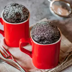 Due tortine in tazza al microonde, ricoperte di zucchero a velo, pronte per essere gustate con due forchettine.