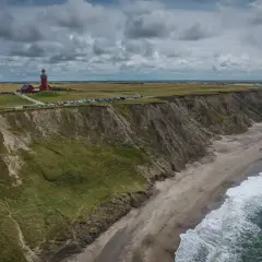 Dania atrakcje: czerwona latarnia morska na klifie, plaża, morze i paralotniarz.