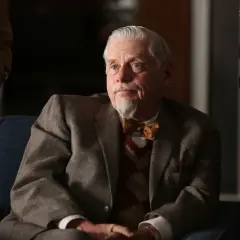 Äldre man med grått hår och bockskägg, klädd i kavaj och fluga. Robert Morse ser fundersam ut.