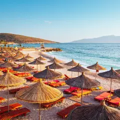 Słoneczna plaża w Albanii w lipcu, pełna parasoli i leżaków, zaprasza do odpoczynku nad turkusowym morzem.