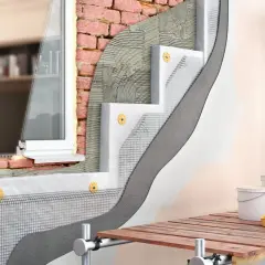 Dettaglio costruttivo di un cappotto termico esterno con isolante, rete e intonaco su una parete in mattoni, vicino a una finestra.