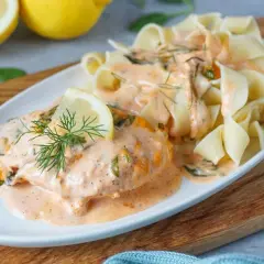 Zartes Lachsfilet in cremiger Sahnesauce mit Spinat, garniert mit Dill und Zitronenspalte, serviert mit breiten Bandnudeln. Ein köstliches Lachs Sahne Gratin.