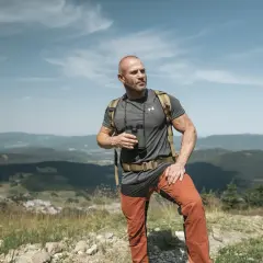 Mężczyzna w letniej czapce w góry, z lornetką w ręku, podziwia krajobraz.