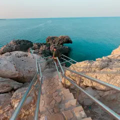 Kamienne schody prowadzą do turkusowego morza na Cyprze, Ayia Napa. Skały i błękit wody tworzą malowniczy krajobraz.