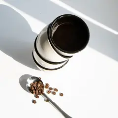 Stos kawy z ekspresu, obok łyżeczka z ziarnami kawy. Zastanawiasz się, ile kofeiny ma kawa z ekspresu?
