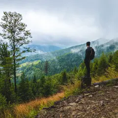 Mężczyzna z plecakiem podziwia widok na górzyste tereny podczas **hiking po polsku**. Mgła spowija szczyty, tworząc malowniczy krajobraz.