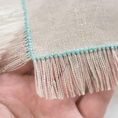 Close-up of a hand holding linen fabric with a turquoise stitched edge, showing how to sew fringe.