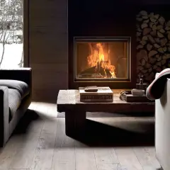 Gemütliches Wohnzimmer mit Kaminfeuer, Holzstapel und Blick auf verschneite Bäume. Tolle Kamin Ideen für Ihr Wohnzimmer.