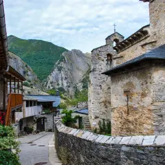 Un pueblo de piedra y madera se alza en el valle del silencio, rodeado de montañas verdes y un cielo nublado.