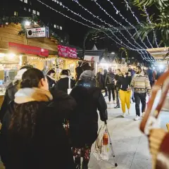 Ambiance féerique d'un marché de Noël à Paris. Des chalets en bois illuminés proposent des spécialités, tandis que des passants flânent sous les guirlandes lumineuses.