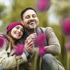 Coppia felice che ride tra i fiori. Un abbraccio sincero, un sorriso contagioso: ecco 15 segnali di una relazione sana.