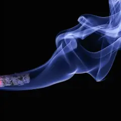 Fumo bluastro si alza da una sigaretta accesa, un'immagine che evoca il pericolo del fumare in allattamento.